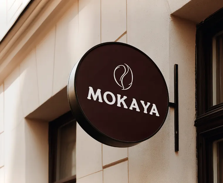 Rundes MOKAYA-Ausleger-Schild an einer hellen Hausfassade